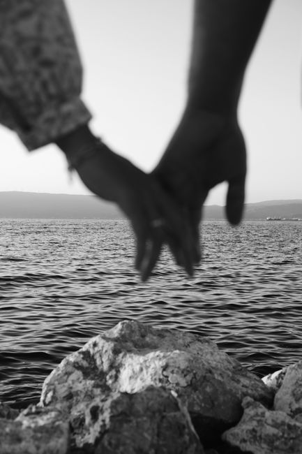 A black and white image of a couple holding hands by the sea.