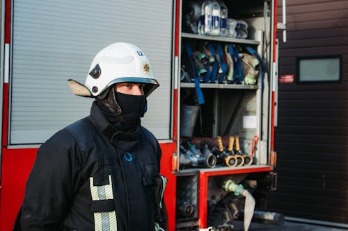 A Firefighter in a Uniform and Helmet Standing near the Firetruck 
