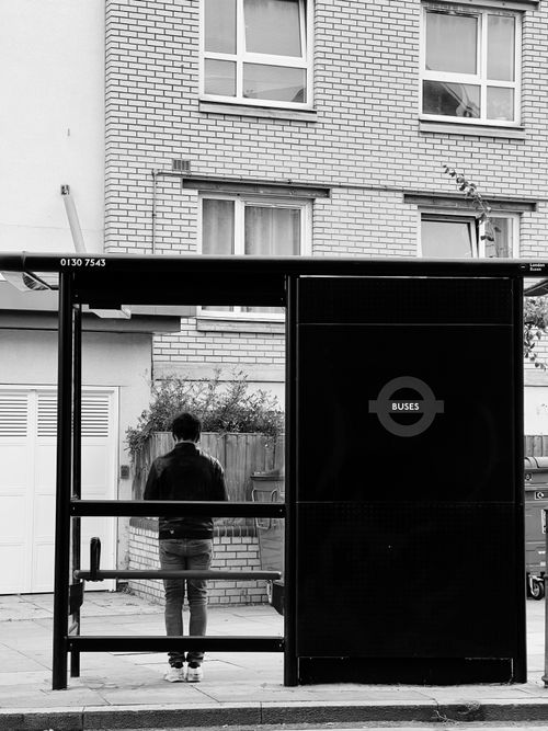 Free Black and white photo of a man waiting at an urban bus stop. Stock Photo