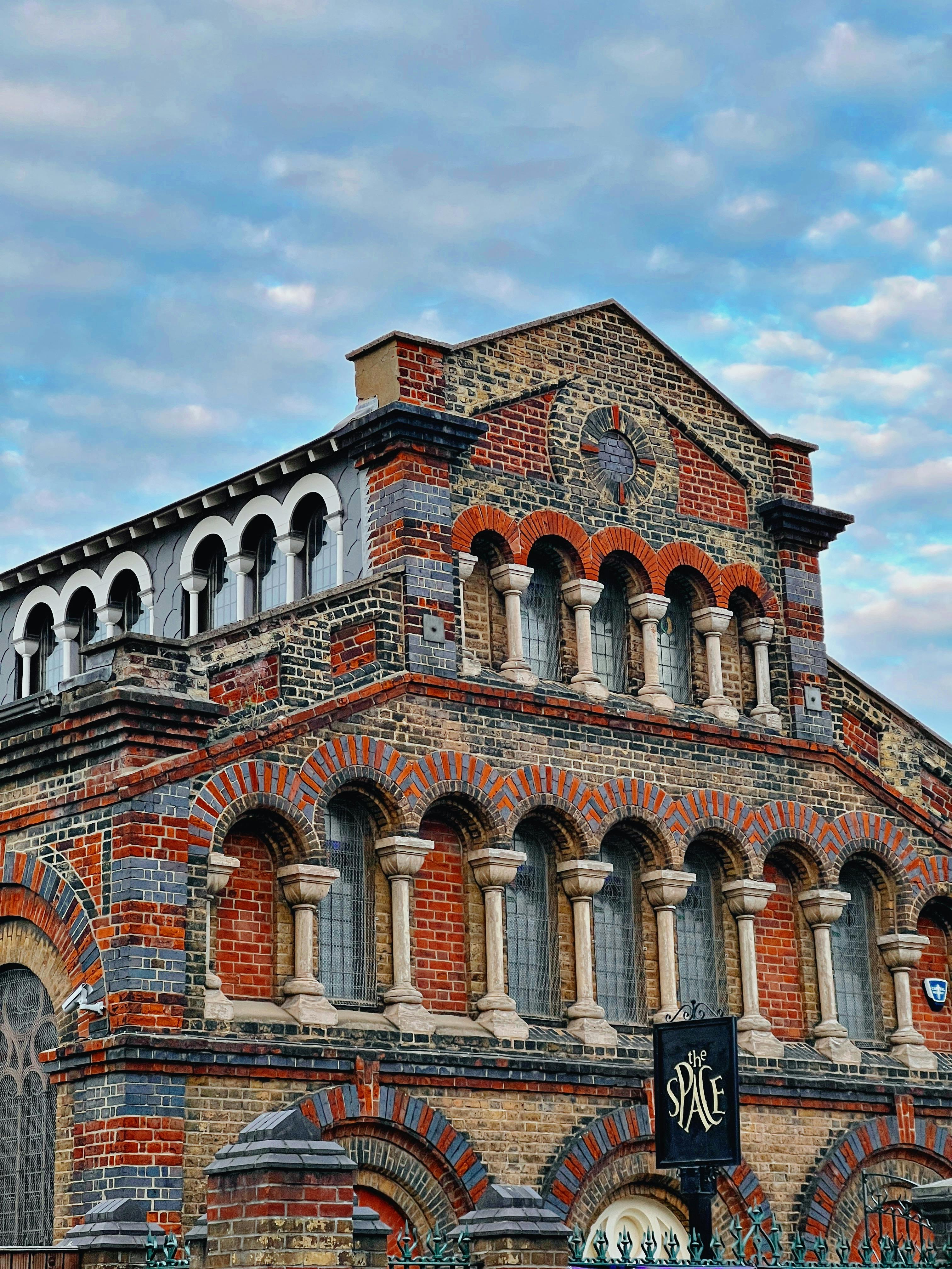 Free Intricate brickwork of a historic building with arched windows under a cloudy sky. Stock Photo