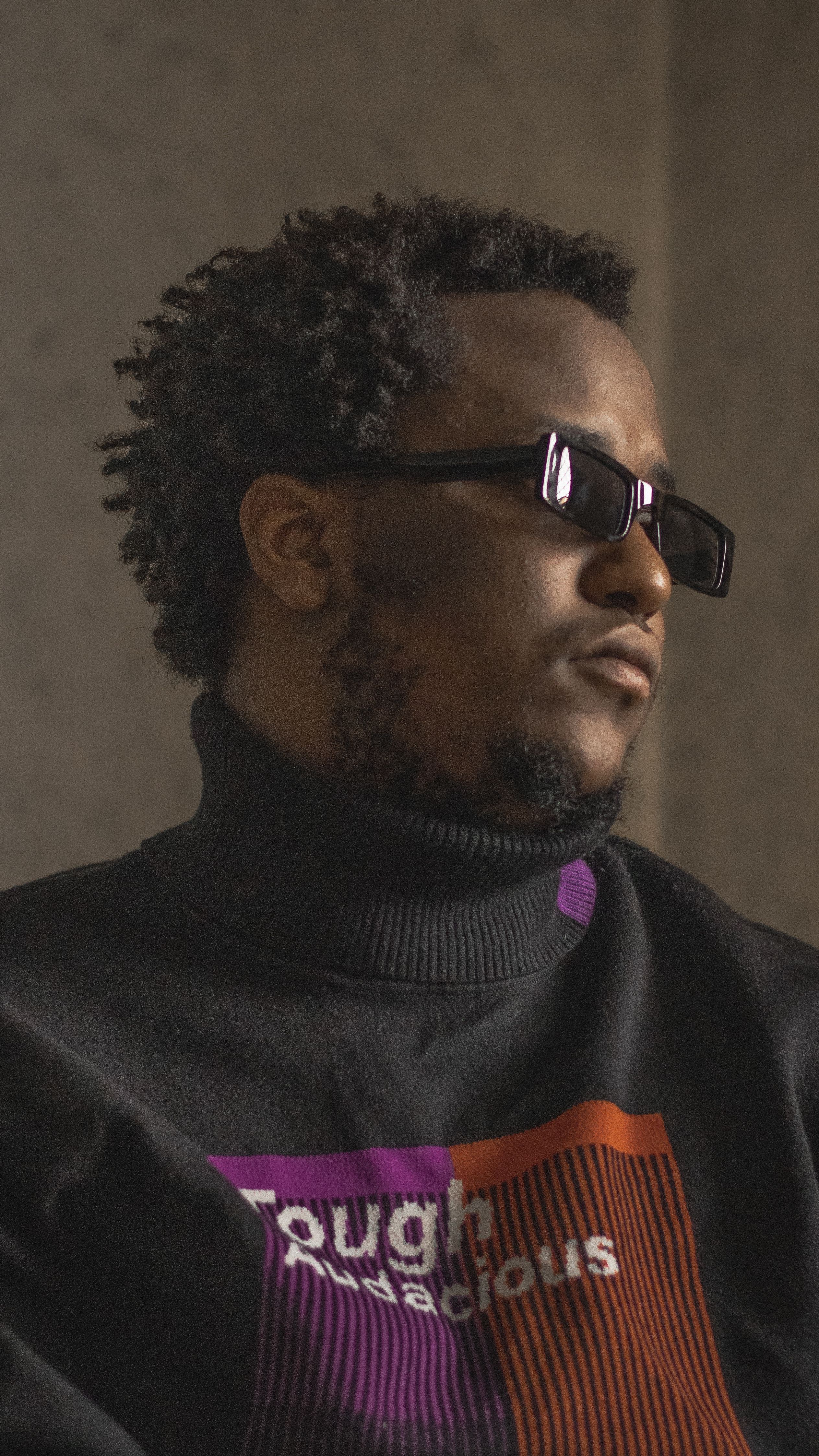 Portrait of a stylish man wearing sunglasses and a turtleneck sweater indoors.
