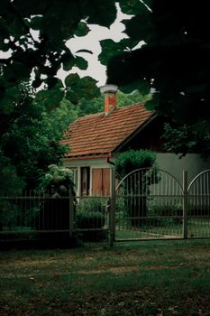 A picturesque cottage surrounded by lush greenery behind a decorative gate.