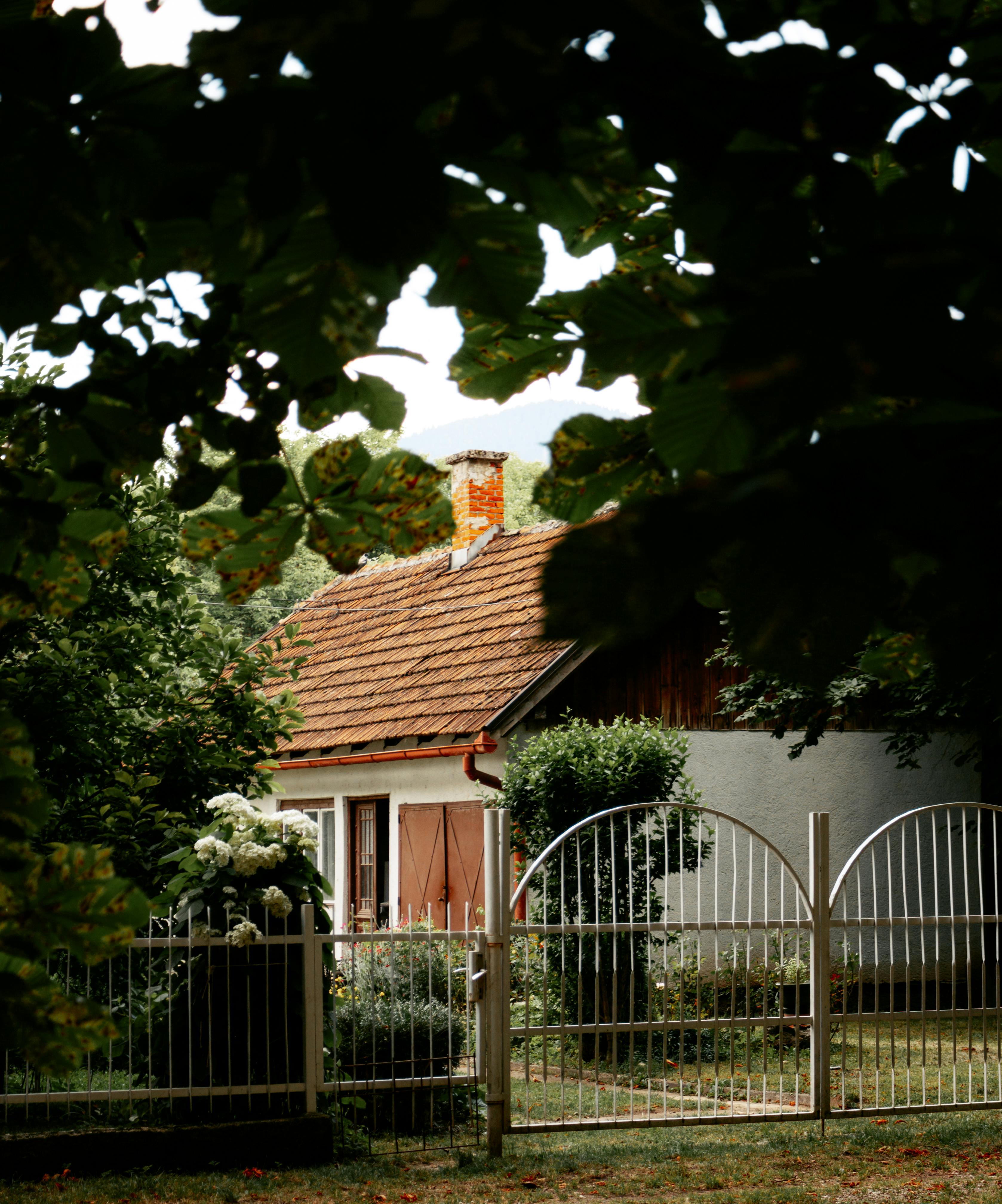 Tranquil rural scene featuring a quaint cottage surrounded by lush greenery behind a decorative fence.