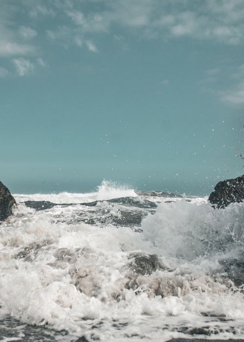 Free Vibrant ocean waves energetically crash over rugged rocks under a clear sky. Stock Photo