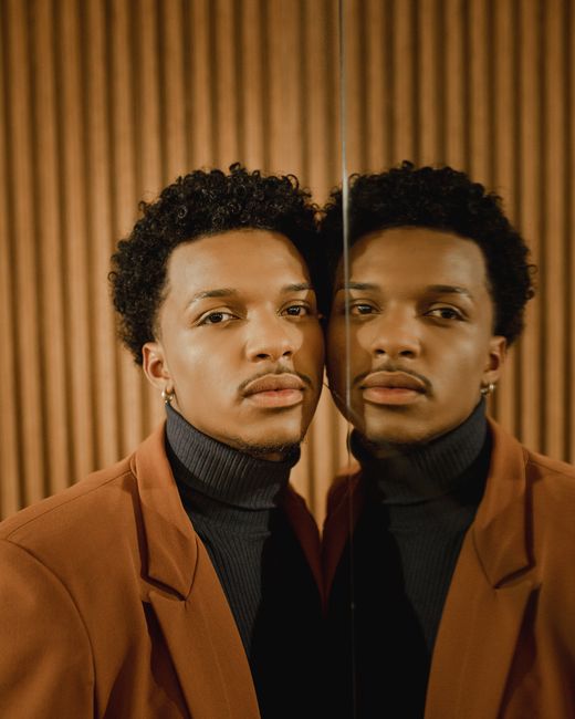 Young man in fashionable attire gazing at his reflection in a mirror.