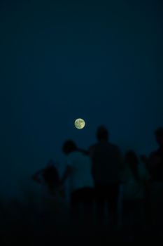 A group silhouette viewing the full moon in a deep blue night sky.