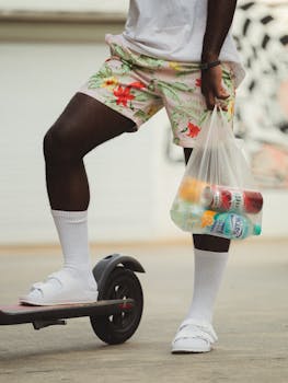 Person in tropical shorts on scooter holding colorful drinks for a summer vibe.