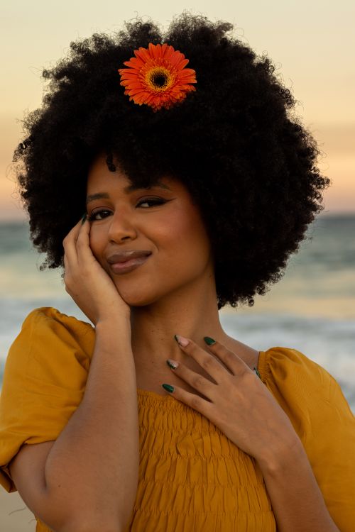 Free A young woman with afro hair and flower posing on the beach at sunset. Stock Photo
