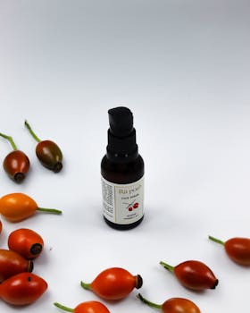 Flat lay of rosehip face serum bottle surrounded by rosehip fruits on a white background.
