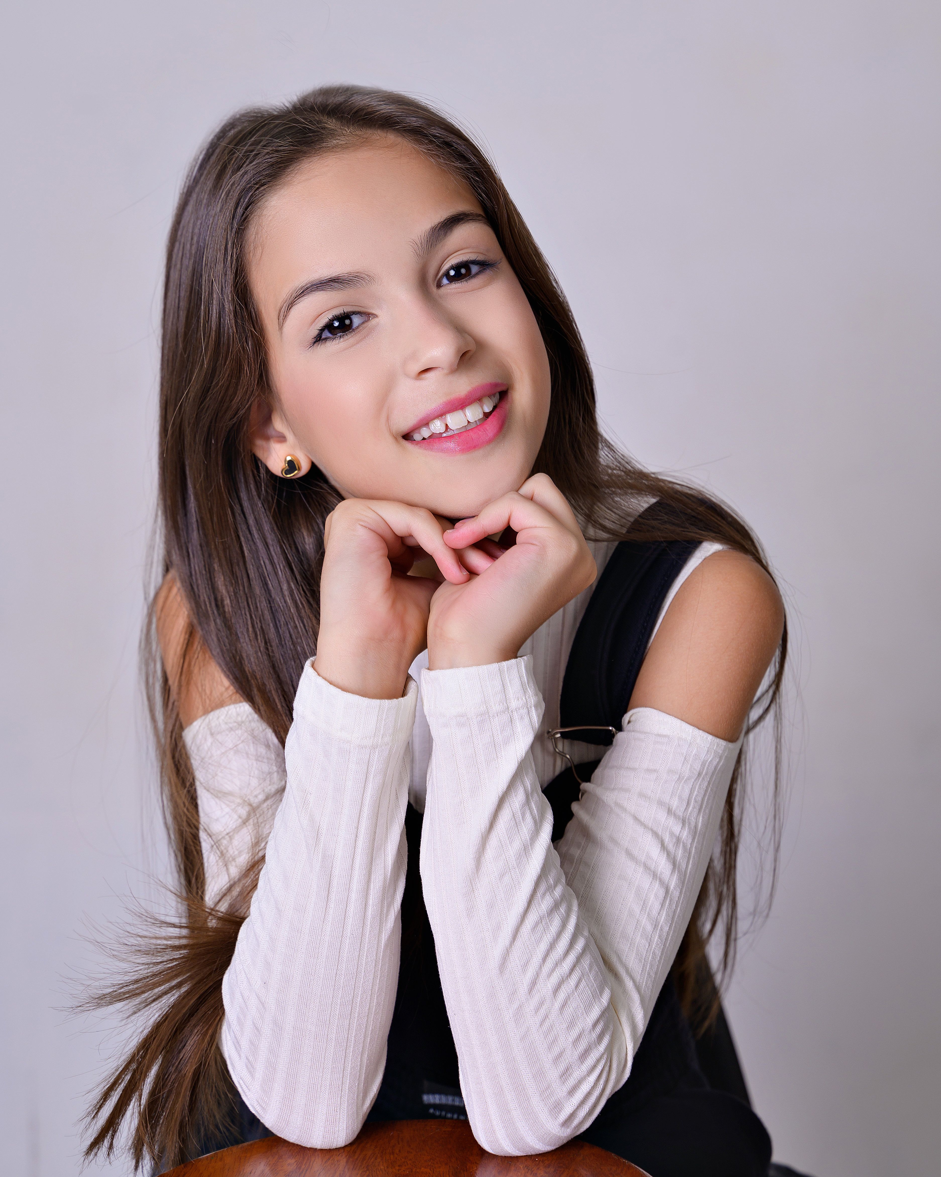 Portrait of a smiling young girl with long hair against a gray background.