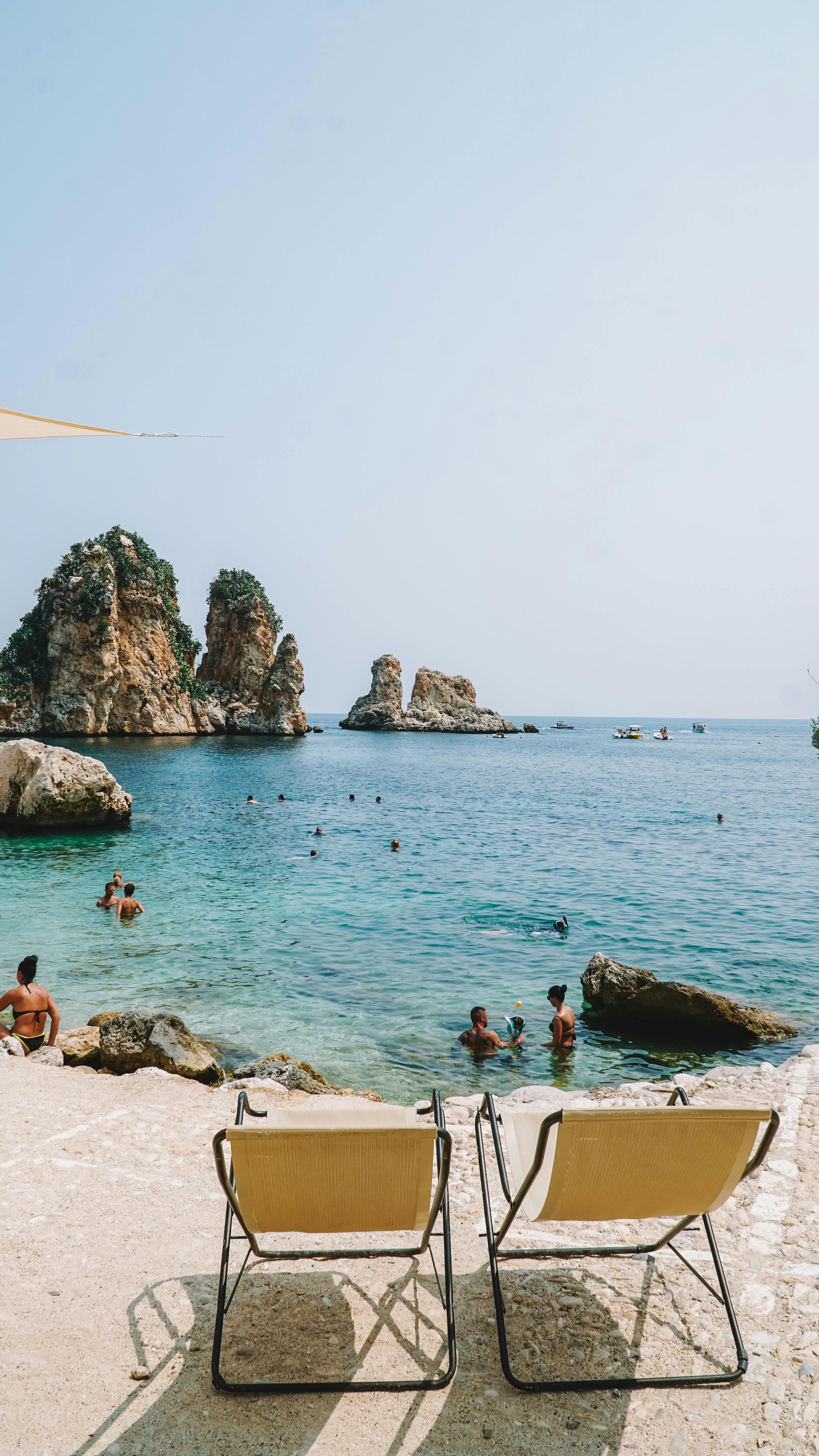 Relaxing beach scene in Scopello, Sicily with crystal clear water and lounging chairs.