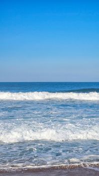 Calming view of ocean waves splashing on the shore under a clear blue sky.
