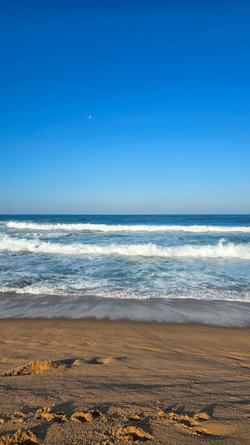 Free Serene sandy beach with gentle waves and a clear blue sky, perfect for summer vibes. Stock Photo