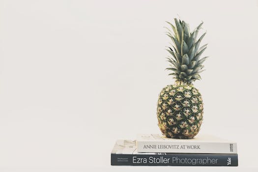 两本堆叠的摄影书上放着一颗菠萝，背景朴素