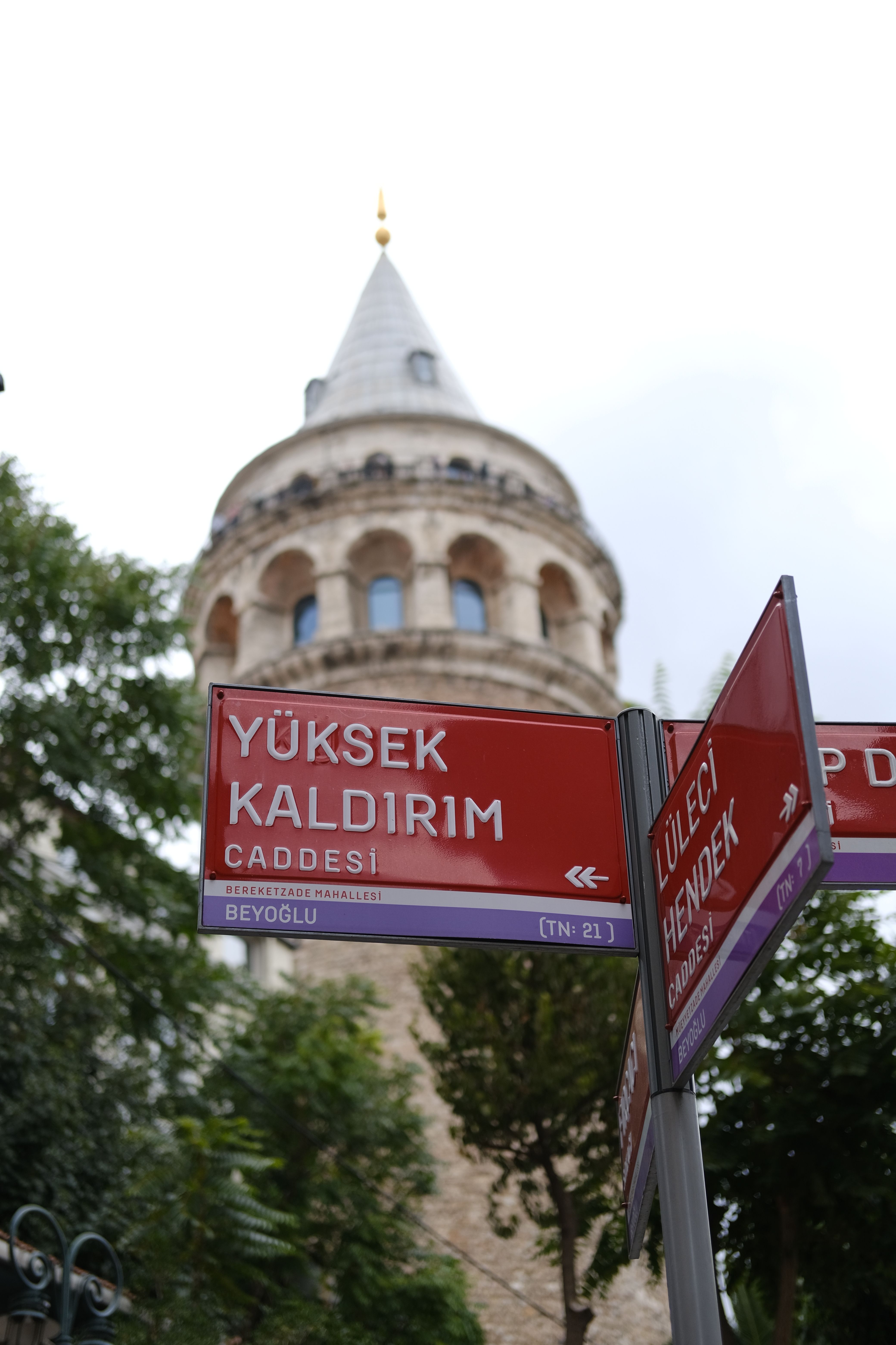 A view of the iconic Galata Tower with street signs in Istanbul, showcasing the historic landmark and urban atmosphere.
