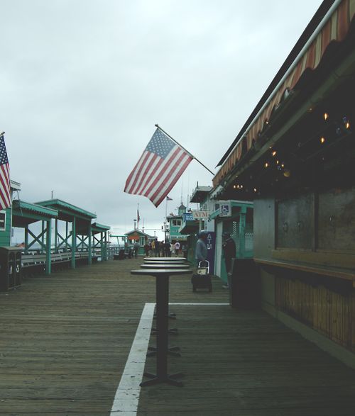 Free American flag waves on a cloudy day at a Los Angeles pier, symbolizing patriotism. Stock Photo