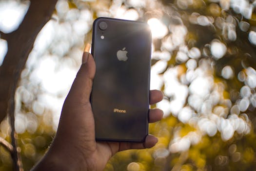A hand holding a smartphone outdoors with bokeh effect in the background.