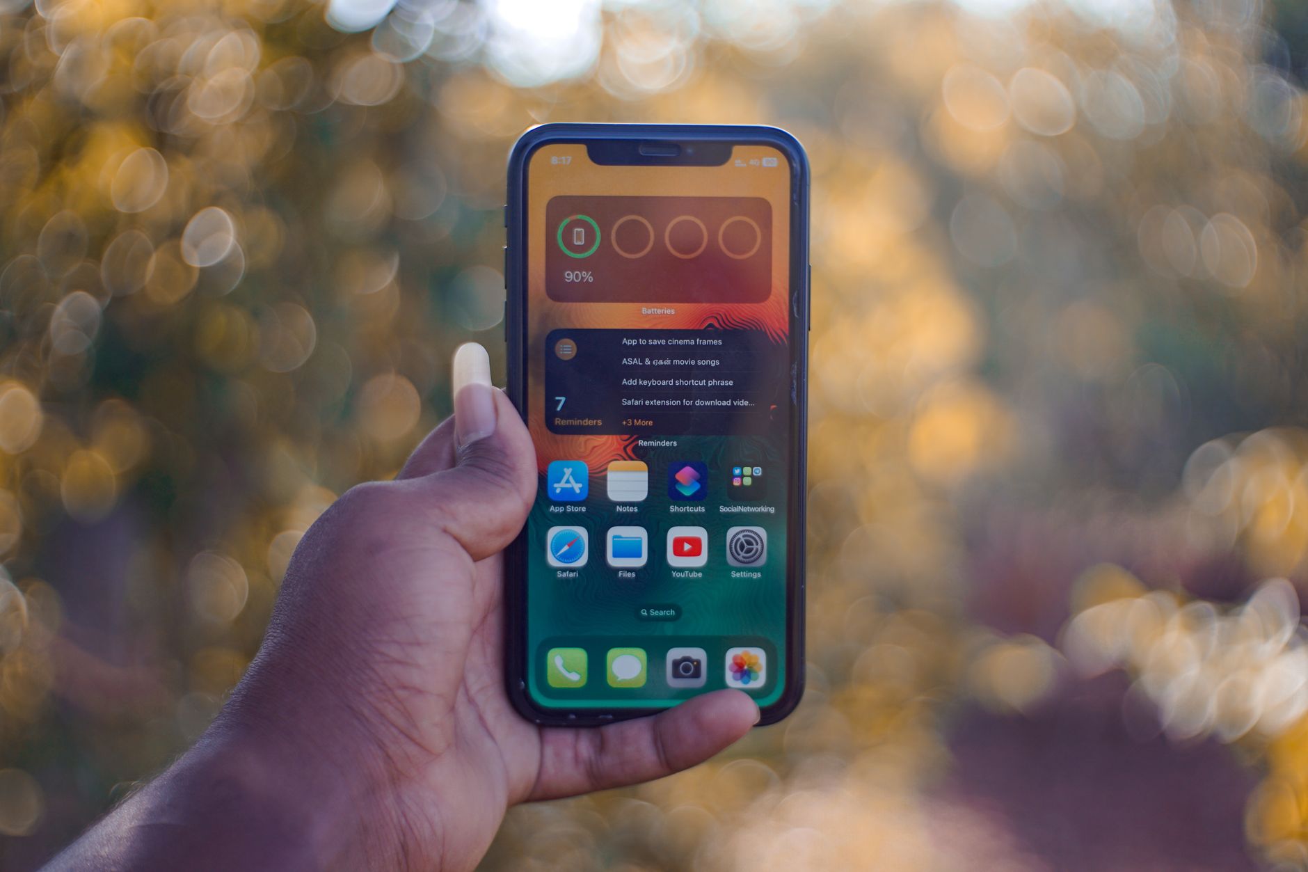 Image of a person's hand holding a smartphone against an outdoor bokeh background.