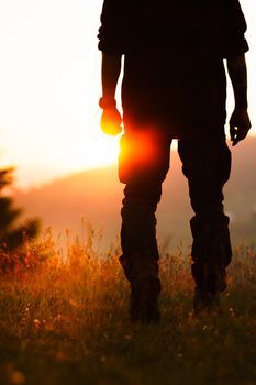 Silhouette of a man standing in a sunlit meadow during sunset, backlit by the glowing sun.
