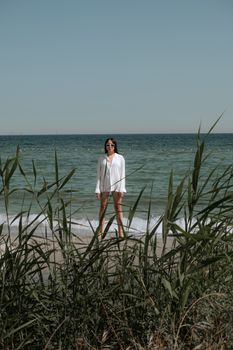 A woman in sunglasses and a white shirt standing on a scenic beach.