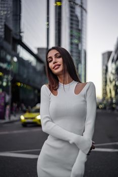Chic woman in white dress poses confidently in a modern city street.
