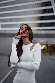 Stylish woman in a white dress posing confidently near a modern building.