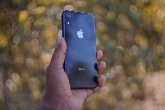 A close-up of a hand holding a smartphone with a blurred outdoor background.