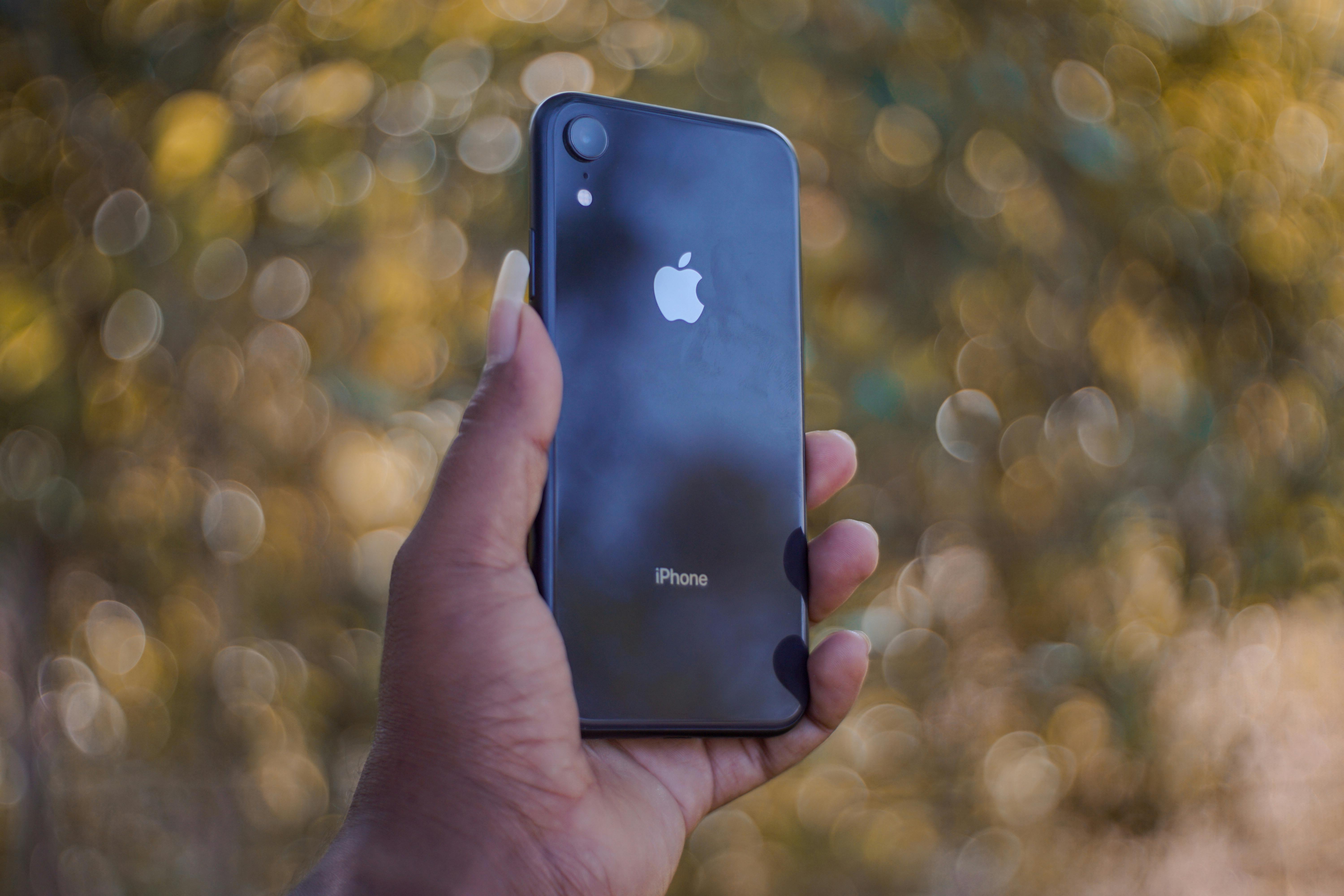 Close-up of a hand holding a smartphone outdoors with a bokeh effect.