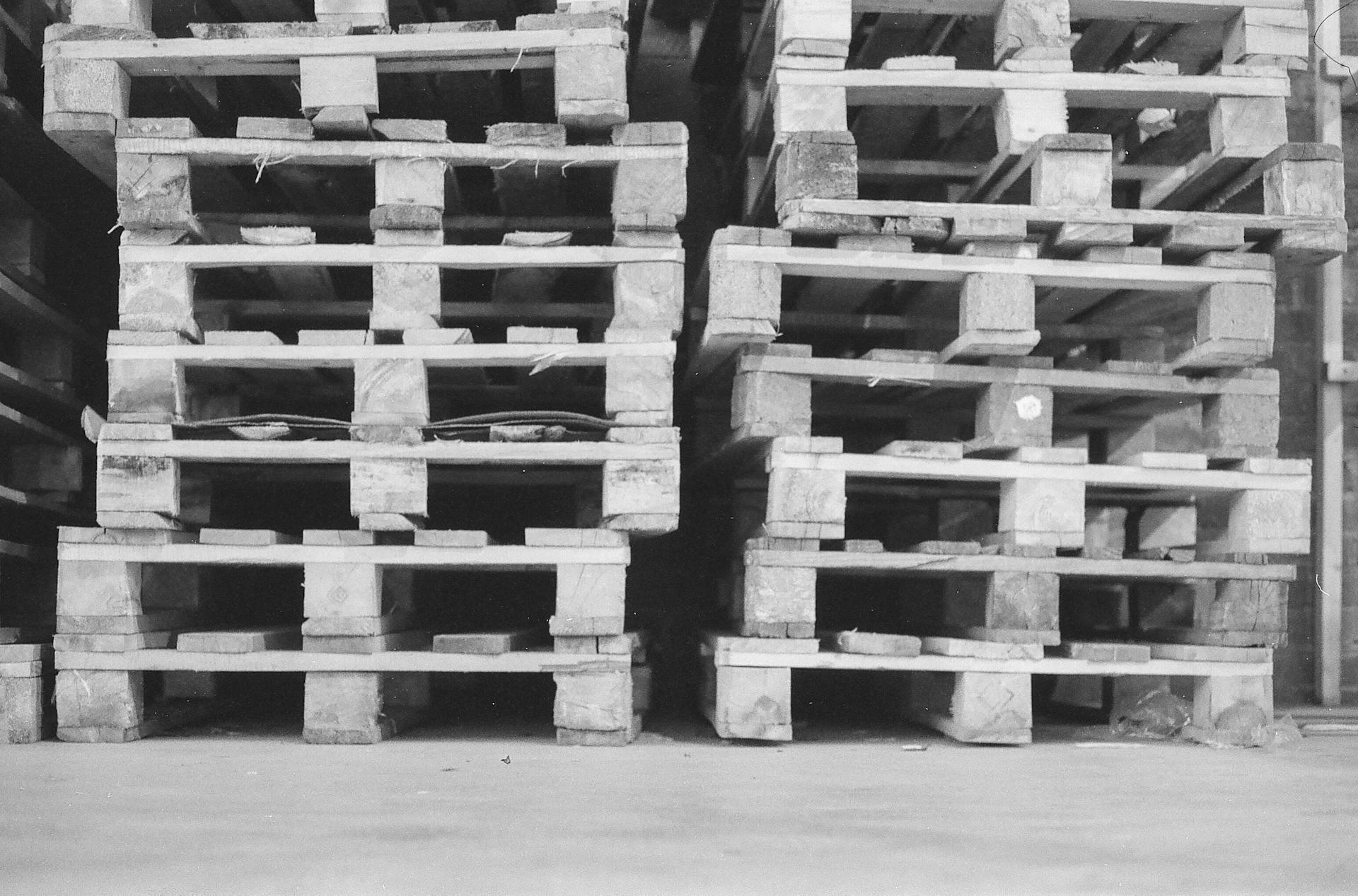 Stacked wooden pallets in a grayscale warehouse setting, emphasizing industrial storage.