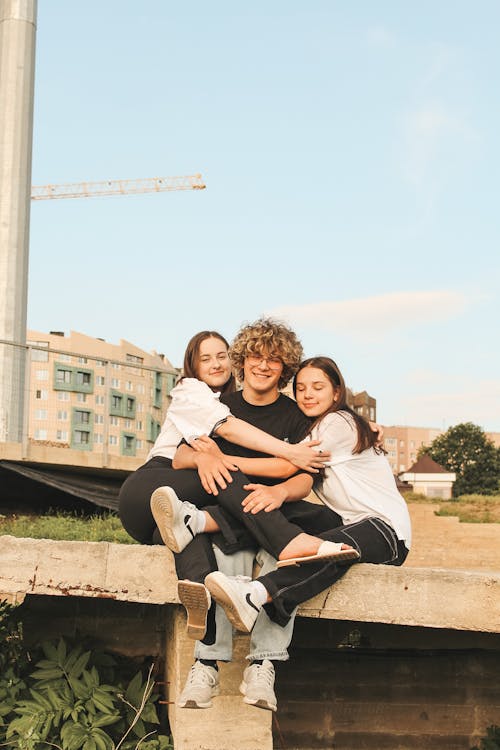 Embracing and Smiling Friends Sitting on Construction Site