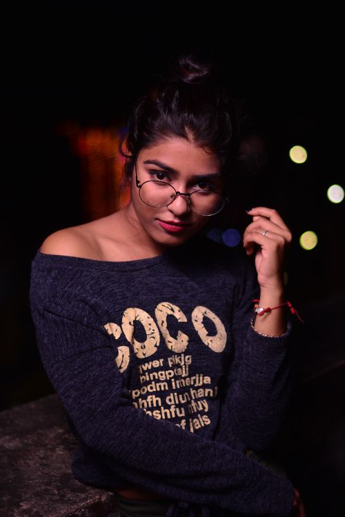 Free Trendy woman posing confidently at night wearing stylish eyewear and sweater. Stock Photo