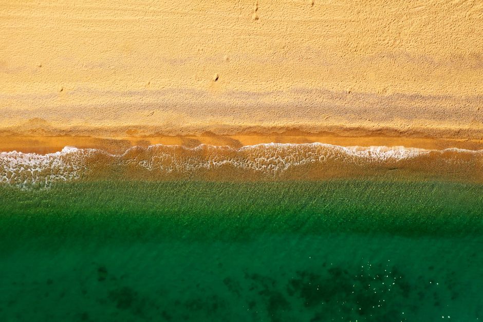 Stunning aerial view of a vibrant sandy beach meeting the emerald sea at Pineda de Mar, España.