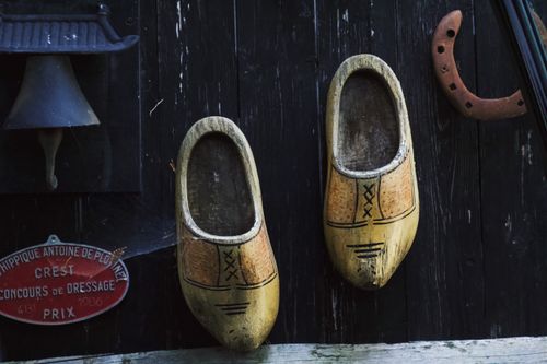 Free Vintage wooden clogs on a rustic wall in Auvergne-Rhône-Alpes, France, beside an antique bell and horseshoe. Stock Photo