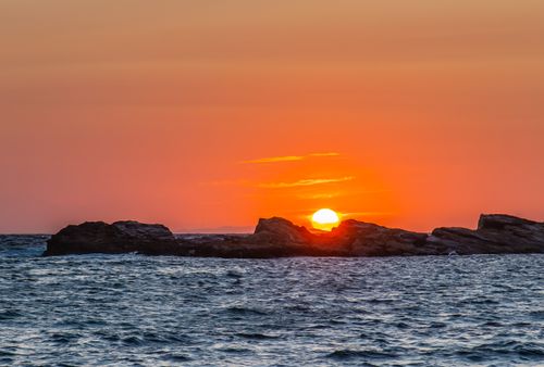 Free A stunning sunset over the rocky sea of Korbous, Tunisia, with a vibrant orange sky. Stock Photo