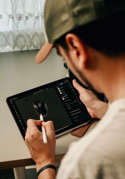 Man sketching a digital portrait on a tablet with a stylus in an indoor setting.