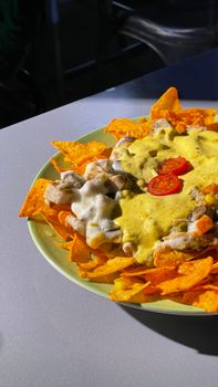 Plate of nachos topped with melted cheese, vegetables, and cherry tomatoes.
