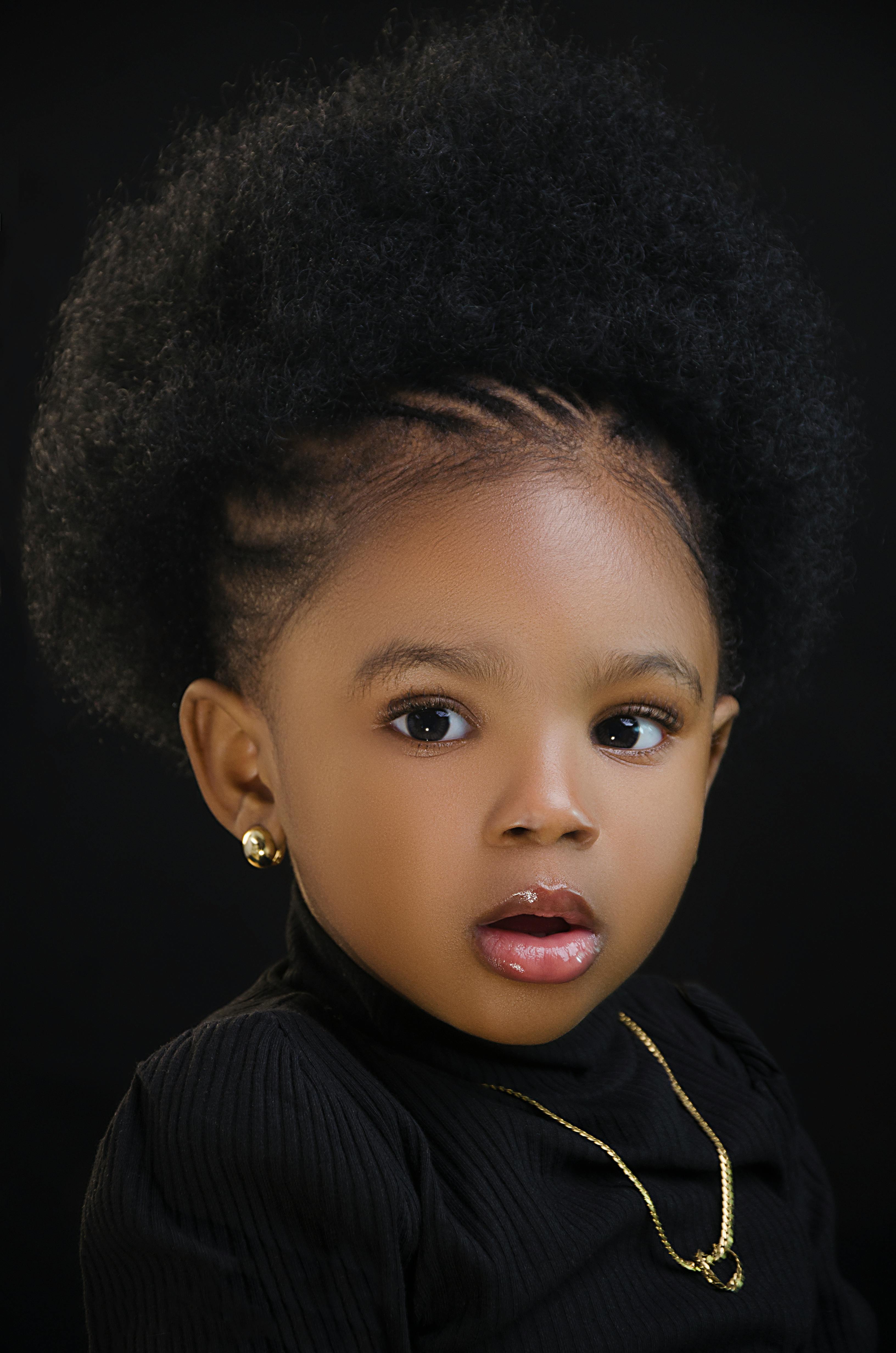Adorable portrait of a young girl with afro hair and gold jewelry in a studio setting.