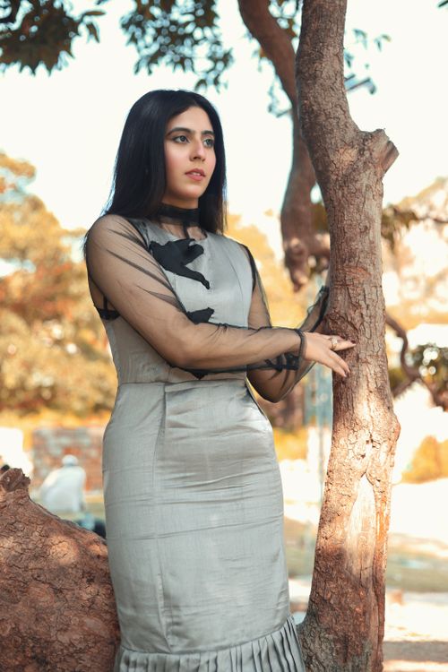 Free A portrait of a woman in a silver dress leaning against a tree in a sunny outdoor setting. Stock Photo