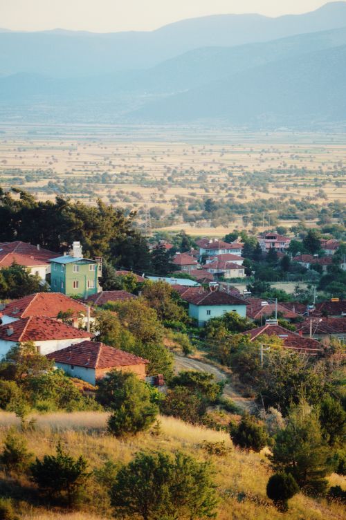 Free Idyllic village with red rooftops nestled in lush countryside with mountains in the background. Stock Photo
