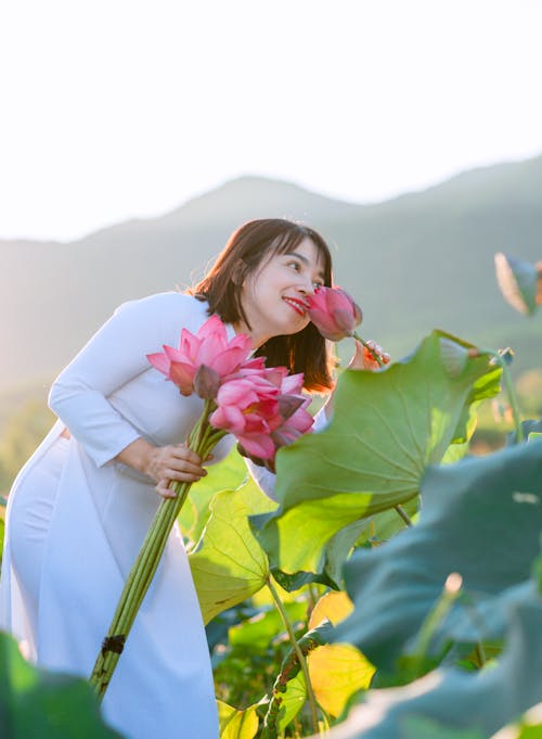 Young woman Smelling a Lotus Flower and Holding a Bouquet 