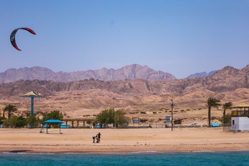 Free Áqaba beach scene with kite surfing and distant mountains, capturing a sunny, wind-filled day. Stock Photo