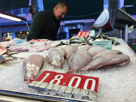 Fresh seafood with price signs displayed on ice at a bustling fish market.