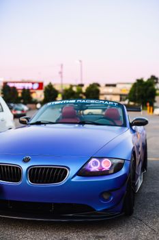 A modern blue convertible sports car parked outdoors with vibrant lights at sunset.