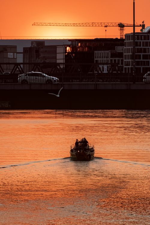 Free Boat glides on river at sunset with city buildings silhouetted in the background. Stock Photo