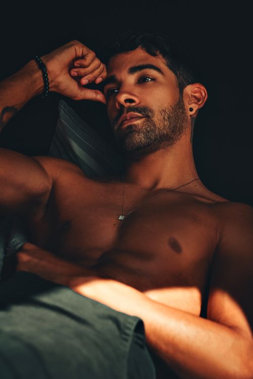 Free Portrait of a shirtless man with stubble posing in shadows, exuding a brooding and athletic vibe. Stock Photo
