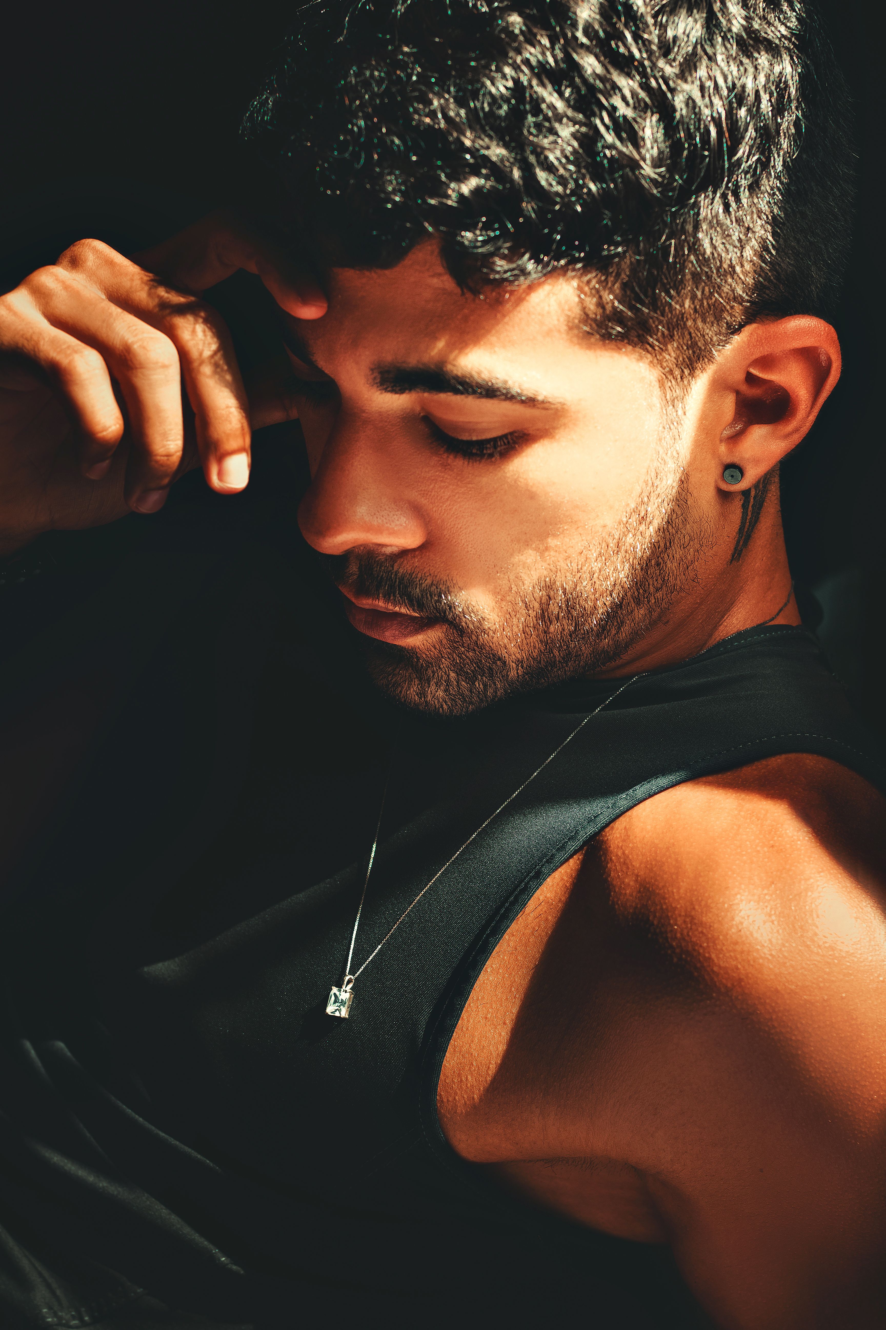 Close-up of a young man in deep thought with sunlight casting dramatic shadows on his face.