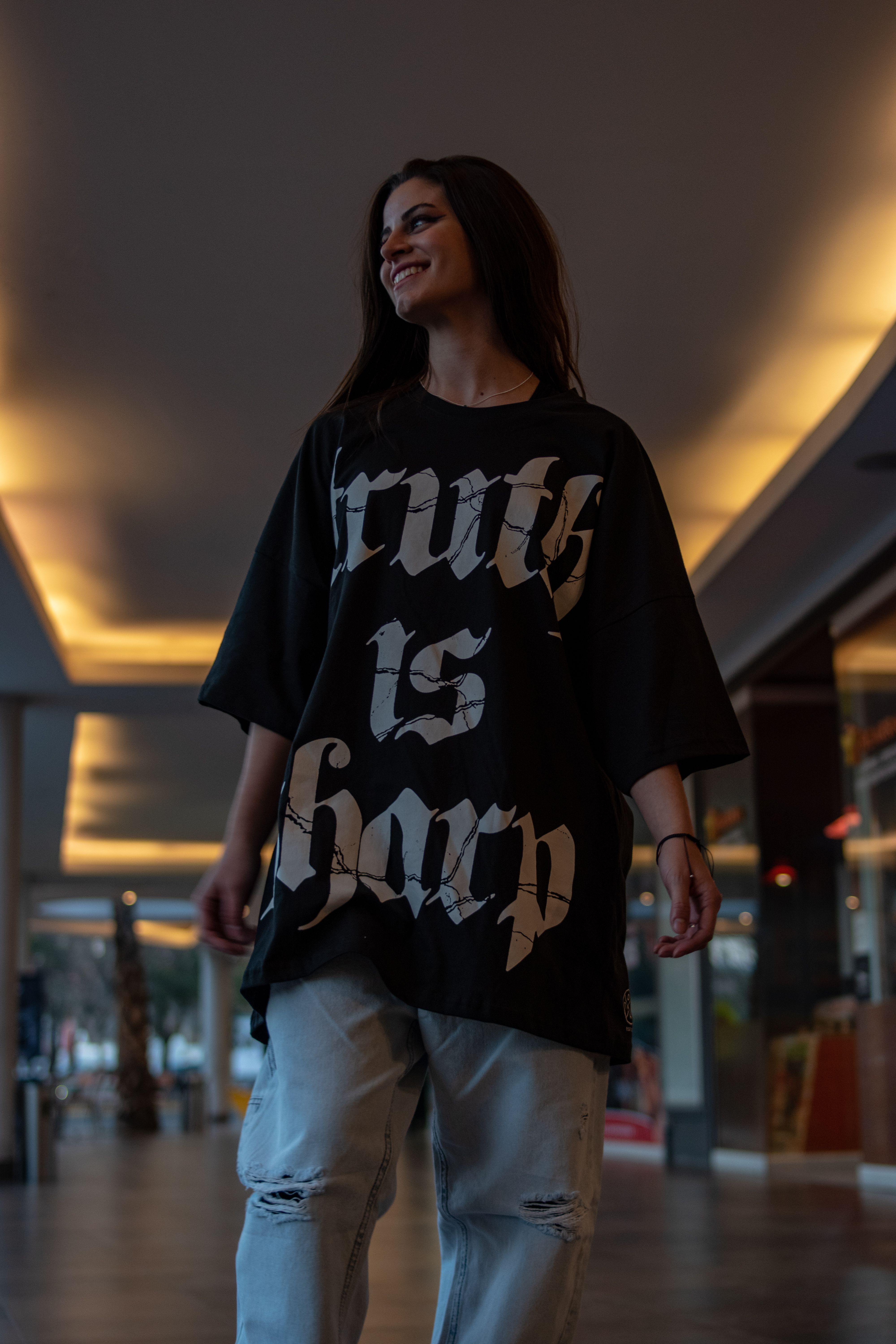 Smiling woman in a black t-shirt with bold text, standing in an urban setting.
