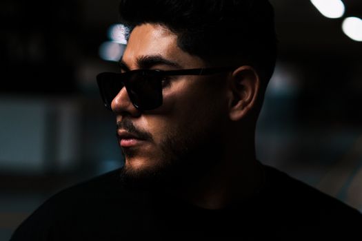 Moody portrait of a man wearing sunglasses, captured in low light for a mysterious look.