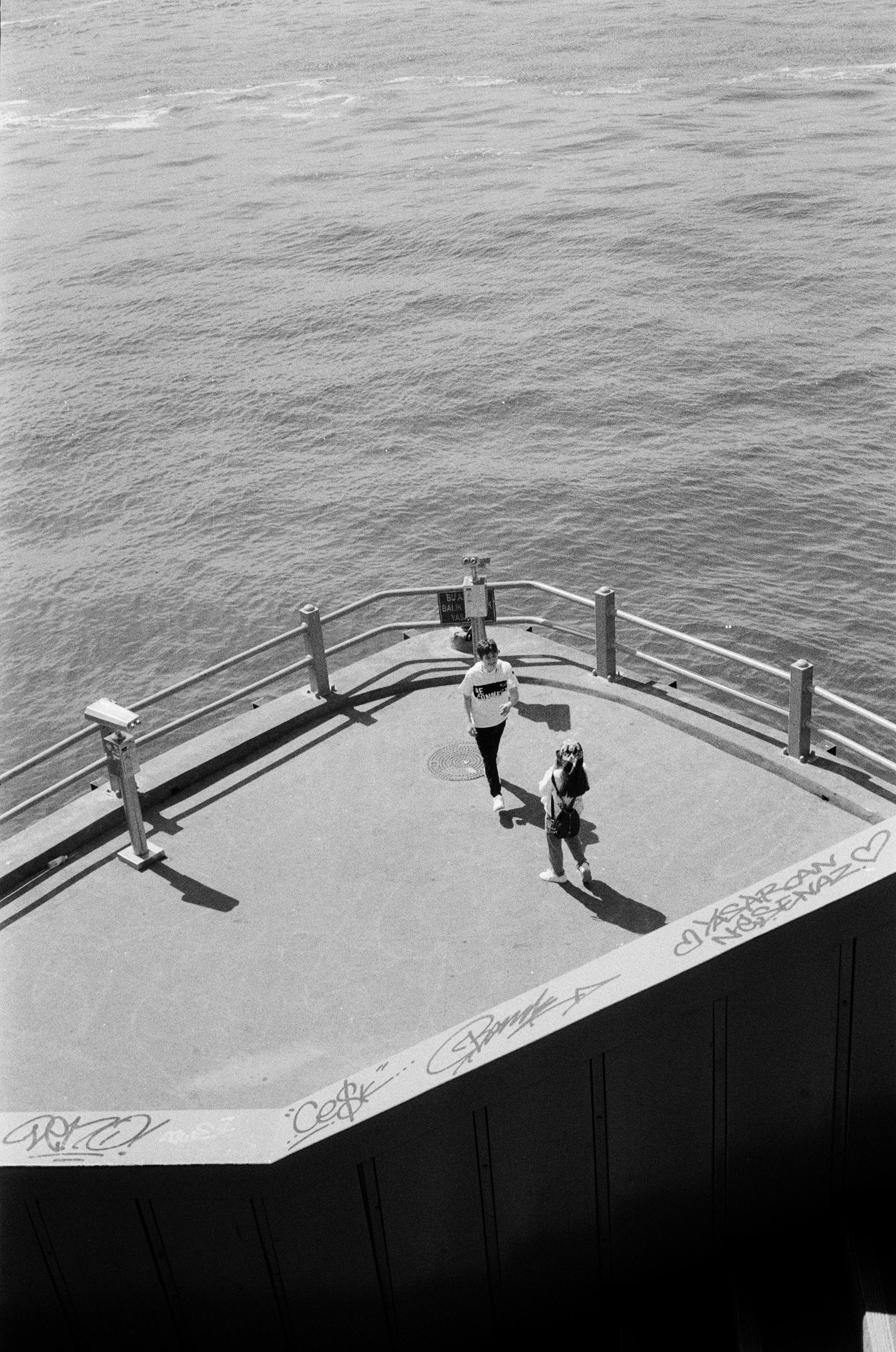 A black and white view of people observing the sea from a pier in İstanbul, Türkiye.