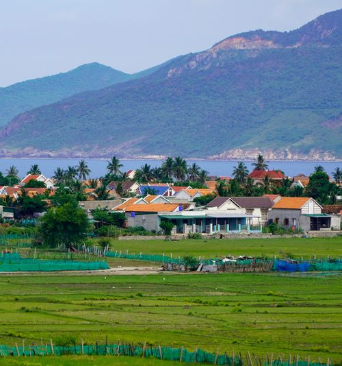 Free Scenic view of a coastal village with colorful houses, palm trees, and mountainous backdrop. Stock Photo